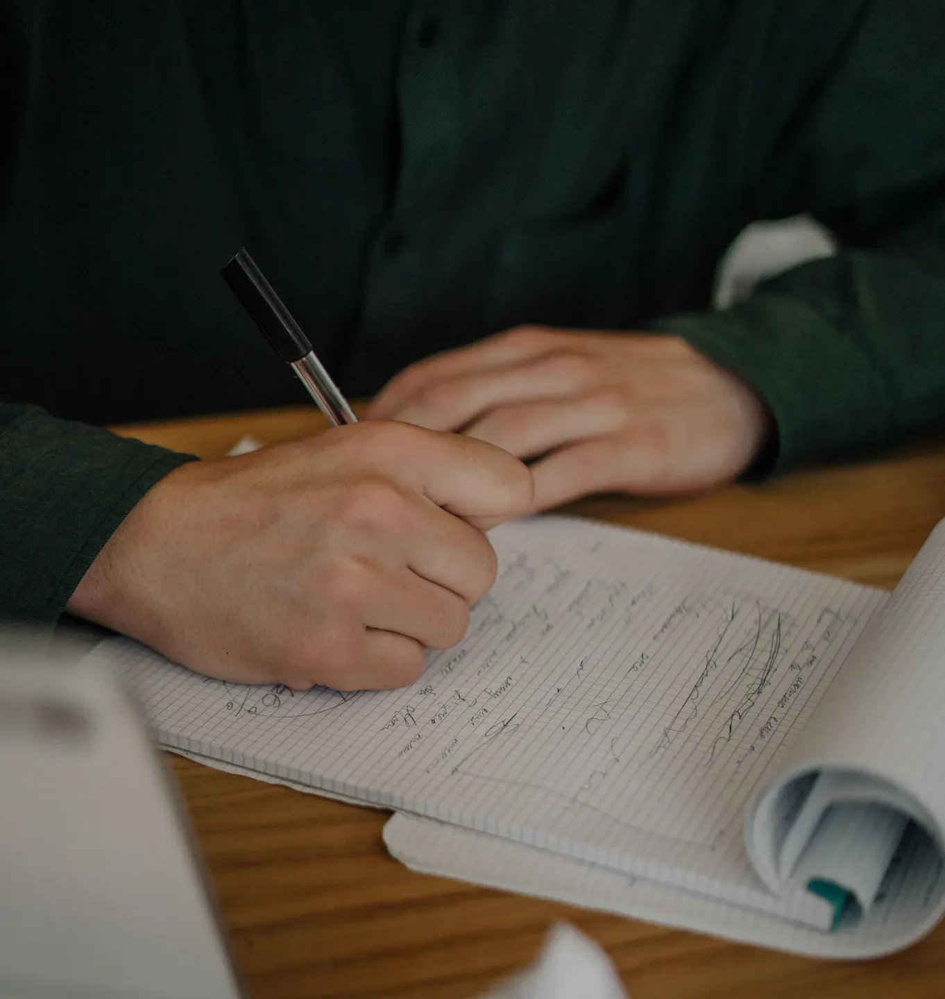 Hands writing in a notebook on a wooden desk, with a paper roll beside it