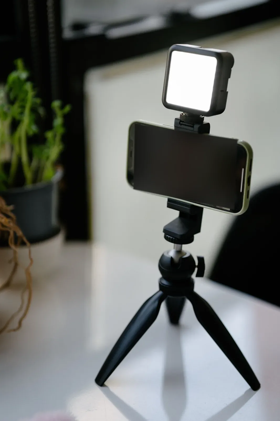 A smartphone on a small tripod with a light panel above it, set up for filming; its screen is dark