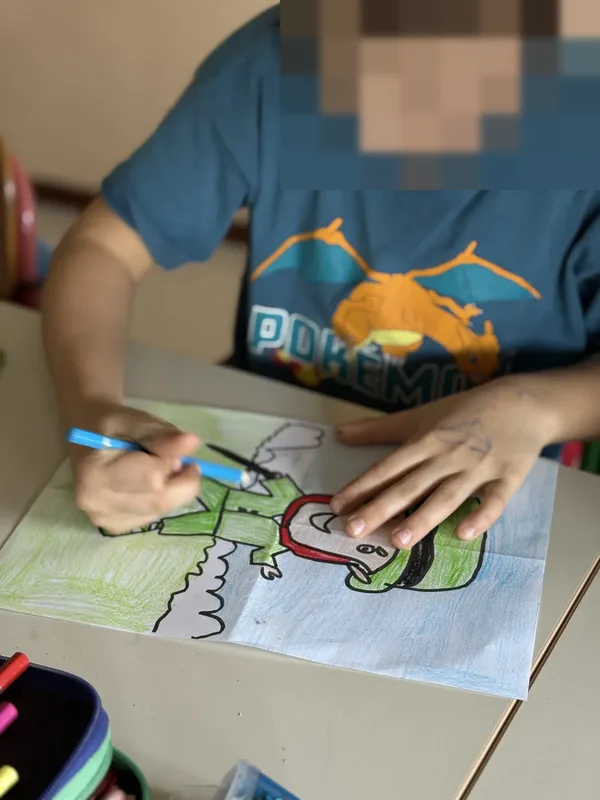 A boy colouring a dragon drawing at his desk.