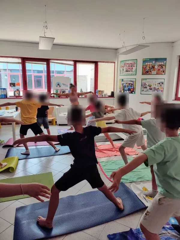 Children holding a yoga warrior pose on mats in a bright classroom.