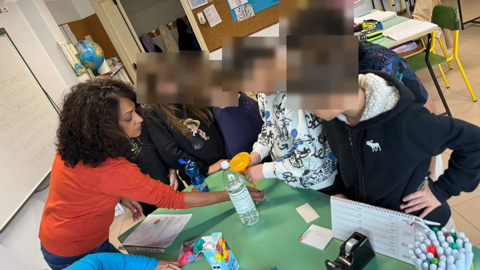 A teacher and a group of pupils around a classroom table, testing a water bottle and a funnel together.