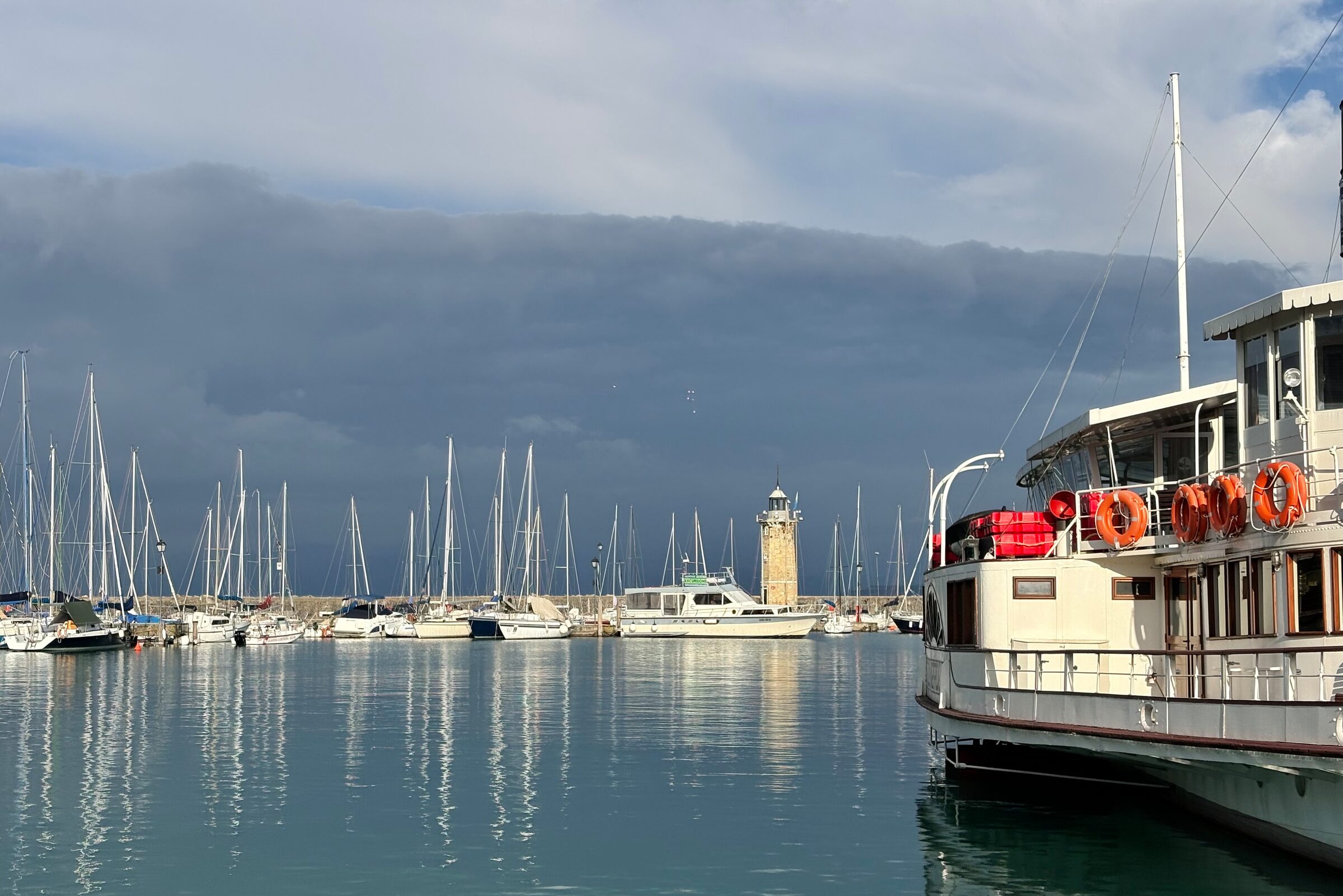 A lake harbour with a lighthouse under a dark, cloudy sky and a white ferry moored on the right.